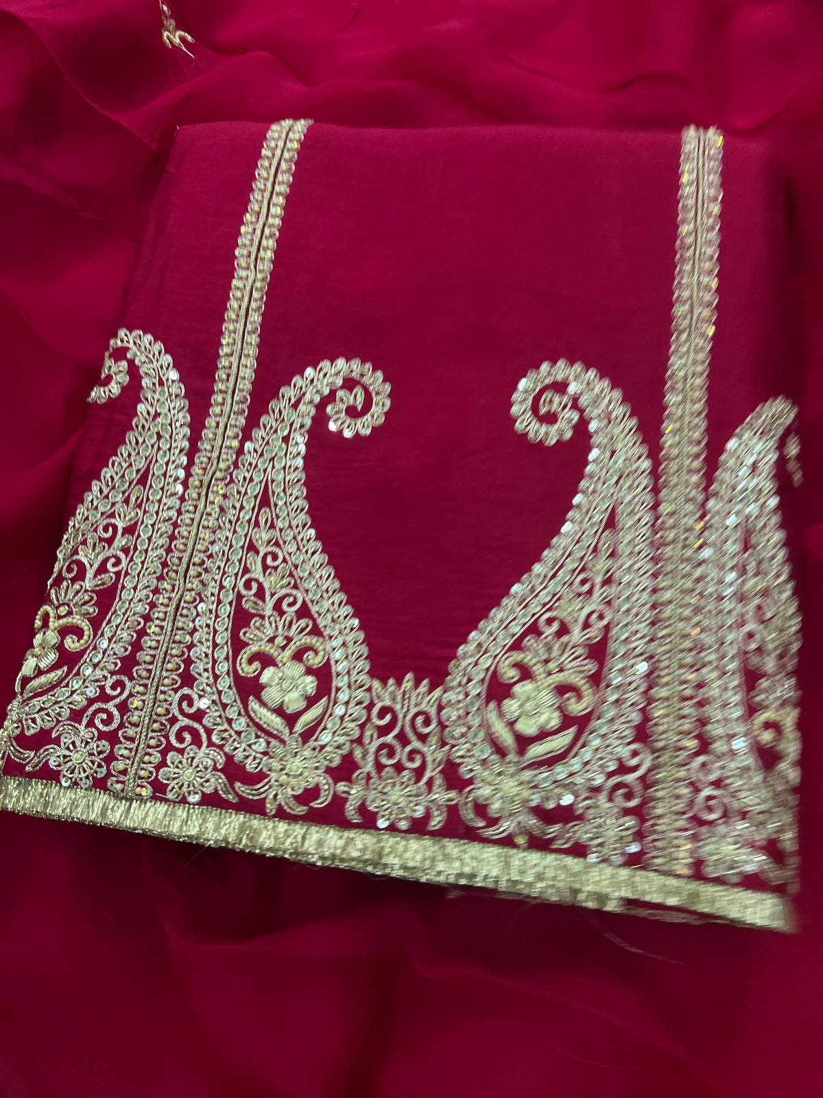 Close-up of gold zari and sequin paisley embroidery on maroon silk suit fabric